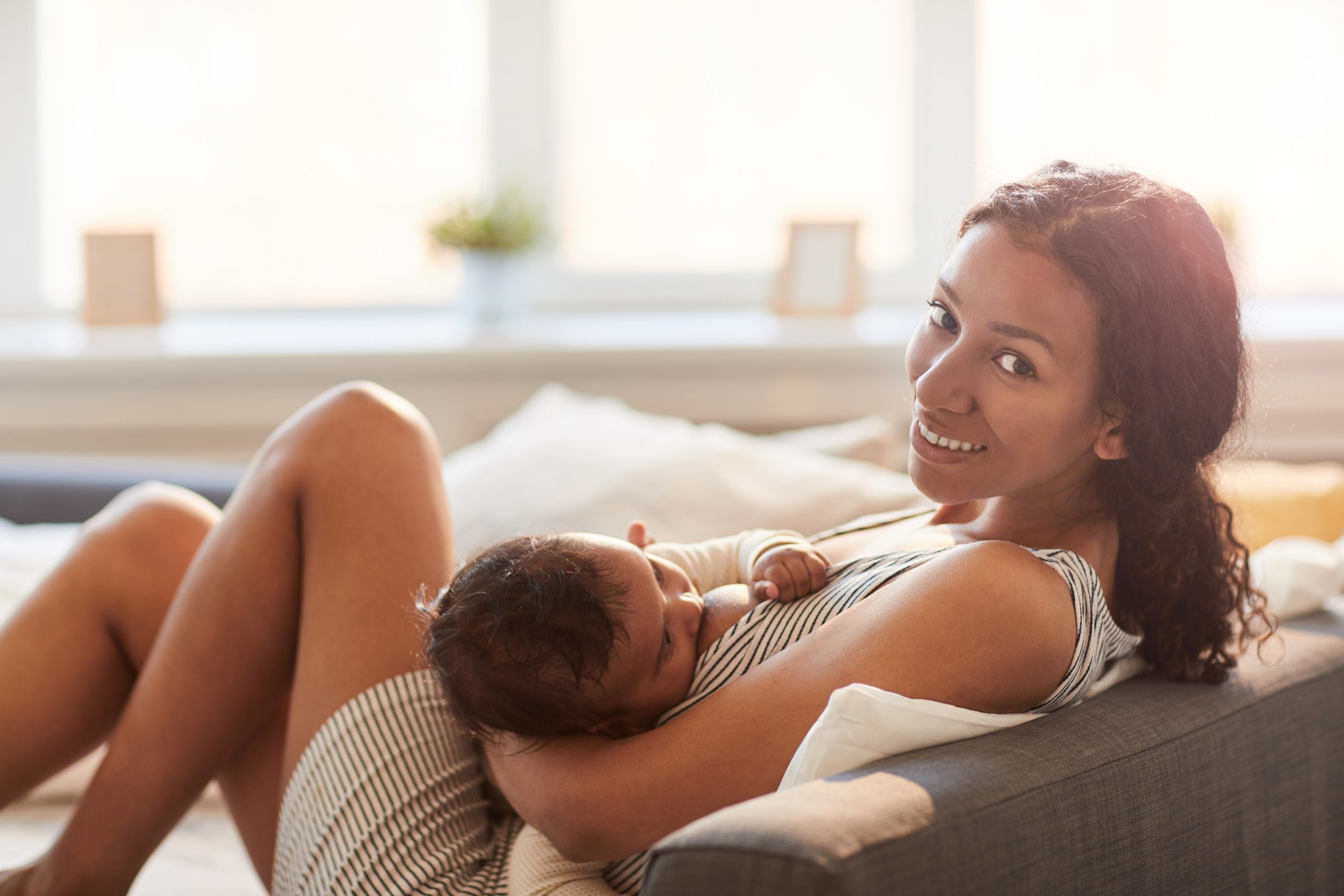 African-American mother breastfeeding baby, smiling, and looking at camera